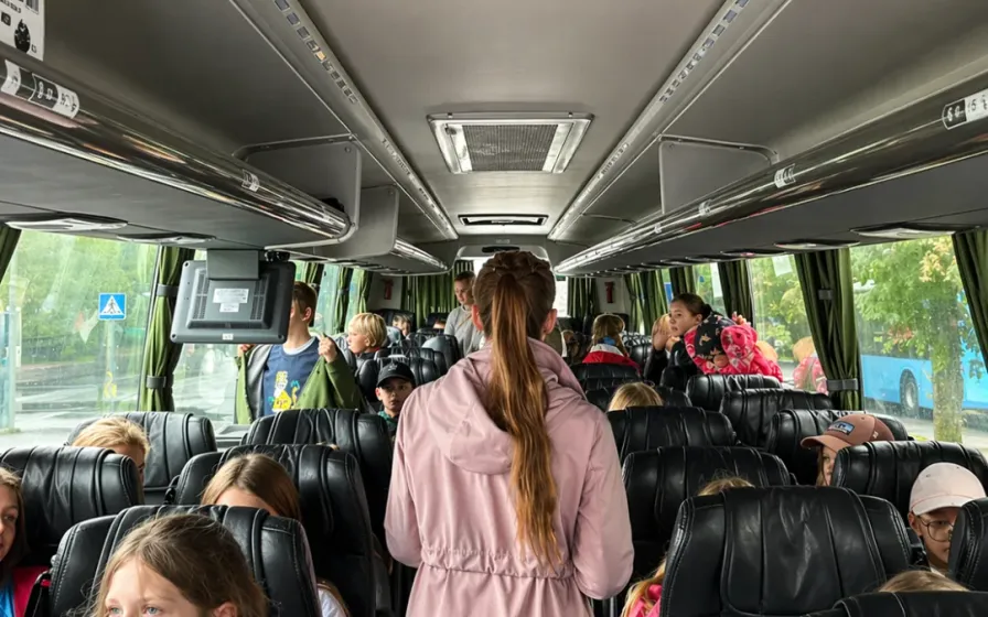 Bussisõidul istuvad lapsed täis istekohtadel, vahekäigus seisab üks täiskasvanu.